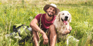 Traveler sitting with golden retriever dog on green meadow