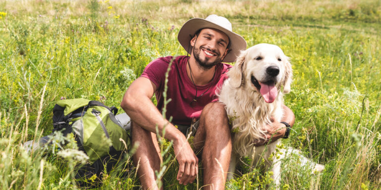 Traveler sitting with golden retriever dog on green meadow