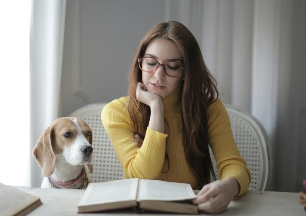 Young woman reading a book with her dog beside her indoors.