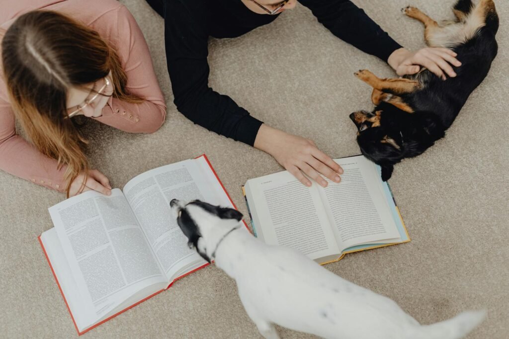Two children reading books on the carpet while playing with cute dogs.