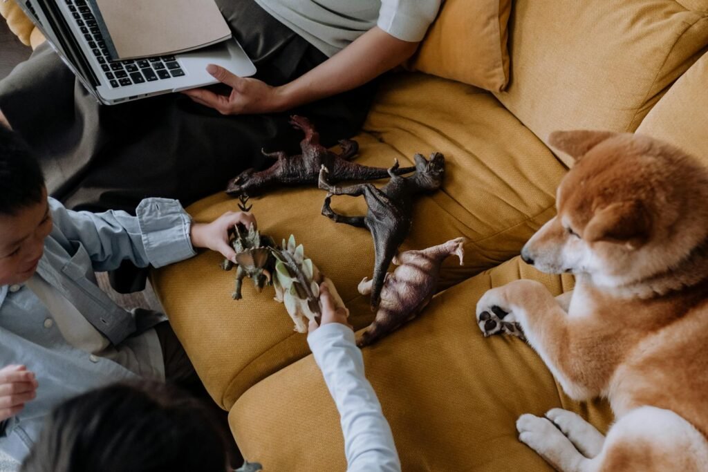 Children playing with dinosaur toys on a sofa while a dog observes. Overhead shot with fun vibe.