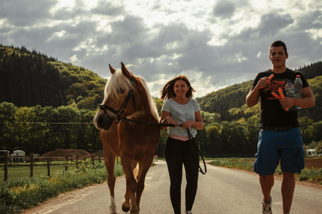 A young couple walking a horse along a scenic country road under a cloudy sky.